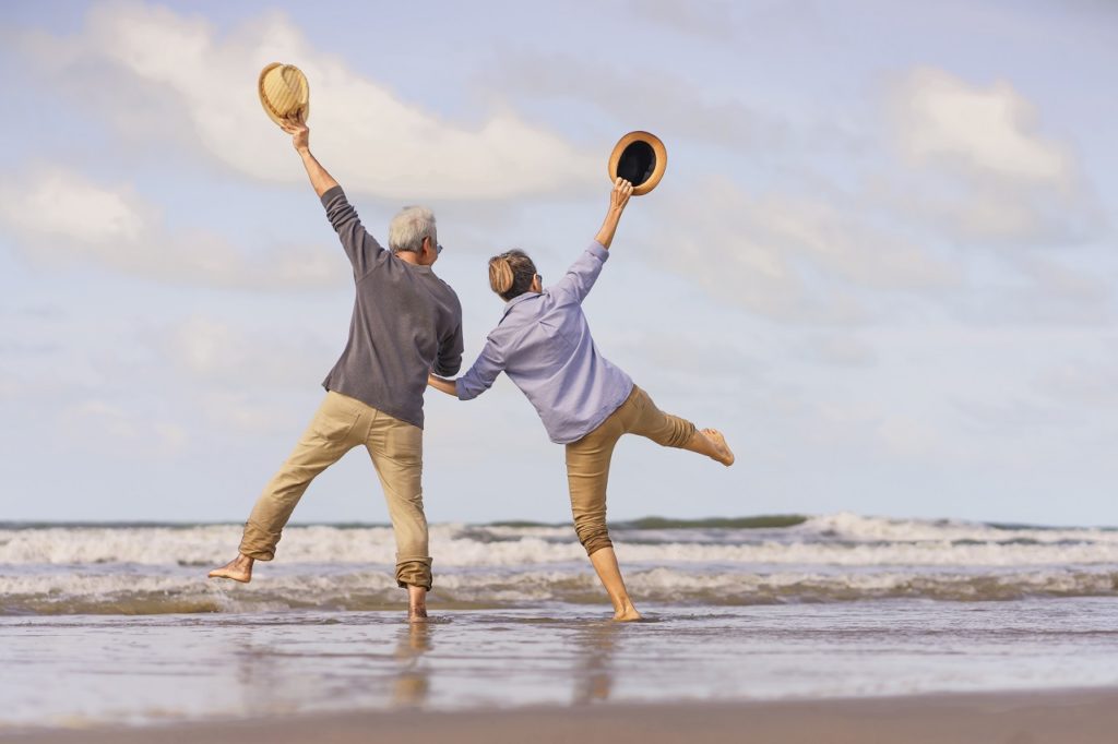 A senior Asian couple jumping at the beach after their retirement